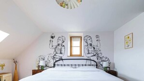 A bedroom with a large bed, a window, and wall art depicting women holding objects. - Logis Marie (flavigny sur Ozerain)