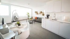 Eine moderne Küche mit weißen Schränken, ein Essbereich mit einem runden Tisch und ein Wohnzimmer mit einer Couch und dekorativen Tellern an der Wand.