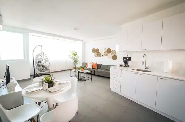 A modern kitchen with white cabinets, a dining area with a round table, and a living room with a sofa and decorative plates on the wall.