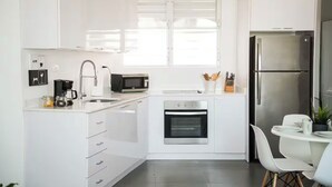 Eine moderne Küche mit weißen Schränken, einem Edelstahlkühlschrank, einer Mikrowelle, einer Kaffeemaschine und einem Essbereich mit weißem Tisch und Stühlen.