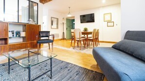 Un salon comprenant une table basse en verre, un canapé, un coin repas avec une table et des chaises, et un téléviseur fixé au mur.