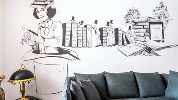A wall with a black and white illustration of a person with a top hat and books, a lamp, and a couch.