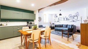 Une cuisine moderne avec des meubles de couleur verte, une table à manger en bois et un canapé bleu dans l’espace salon.