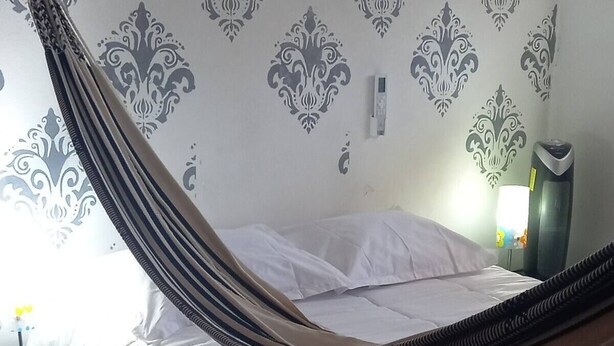 A bed with a striped canopy, a bedside table with a lamp, and a wall with patterned wallpaper. - 2 bedroom apartment - Manga Cartagena Colombia (Cartagena de Indias)
