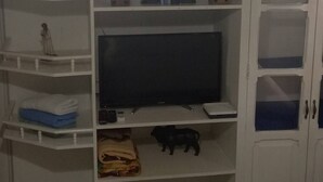 A room with a white entertainment unit containing a flat-screen TV, shelves with various items, and a small cabinet with glass doors. - 2 bedroom apartment - Manga Cartagena Colombia (Cartagena de Indias)