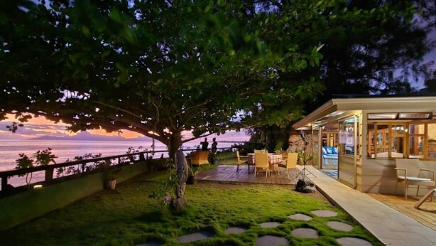 A patio area with a view of the sunset over the water, a tree, and outdoor seating.