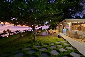 Een terras met uitzicht op de zonsondergang over het water, een boom en buitenmeubilair.