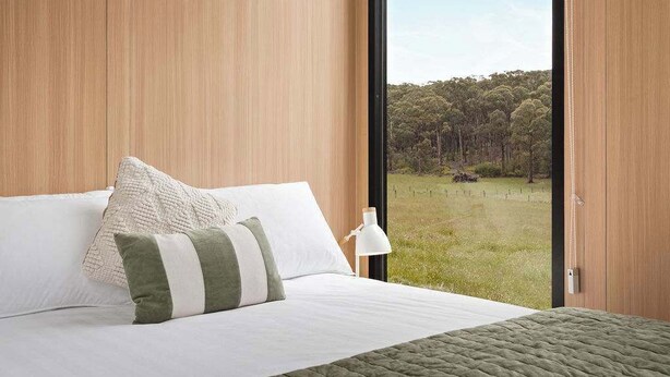 A bedroom with a large window, a bed with white and green bedding, and a view of a forested area. - Paddock & Peak by Tiny Away (Wesburn)