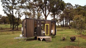 A small cabin with a sliding door, a wooden deck, and a chair outside. - Paddock & Peak by Tiny Away (Wesburn)