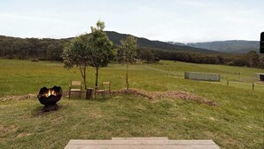 A grassy outdoor area with a fire pit, wooden deck, and chairs. - Paddock & Peak by Tiny Away (Wesburn)