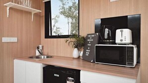 A compact kitchen with a microwave, toaster, and a coffee maker. There's a window with a view of trees and a shelf with glasses. - Paddock & Peak by Tiny Away (Wesburn)