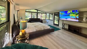 A modern bedroom with a large bed, a TV, and a view of the outdoors through large windows. - Award Winning Home! BBQ-Heated Pool-2 miles from beach (Fort Lauderdale)