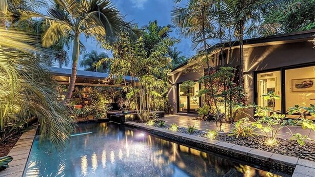 A modern house with a swimming pool surrounded by tropical plants and a well-lit patio area. - Award Winning Home! BBQ-Heated Pool-2 miles from beach (Fort Lauderdale)
