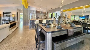 A modern kitchen with a central island, pendant lighting, and a dining area with a long table. - Award Winning Home! BBQ-Heated Pool-2 miles from beach (Fort Lauderdale)
