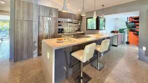 A modern kitchen with a central island, stainless steel appliances, pendant lighting, and a large window. - Award Winning Home! BBQ-Heated Pool-2 miles from beach (Fort Lauderdale)