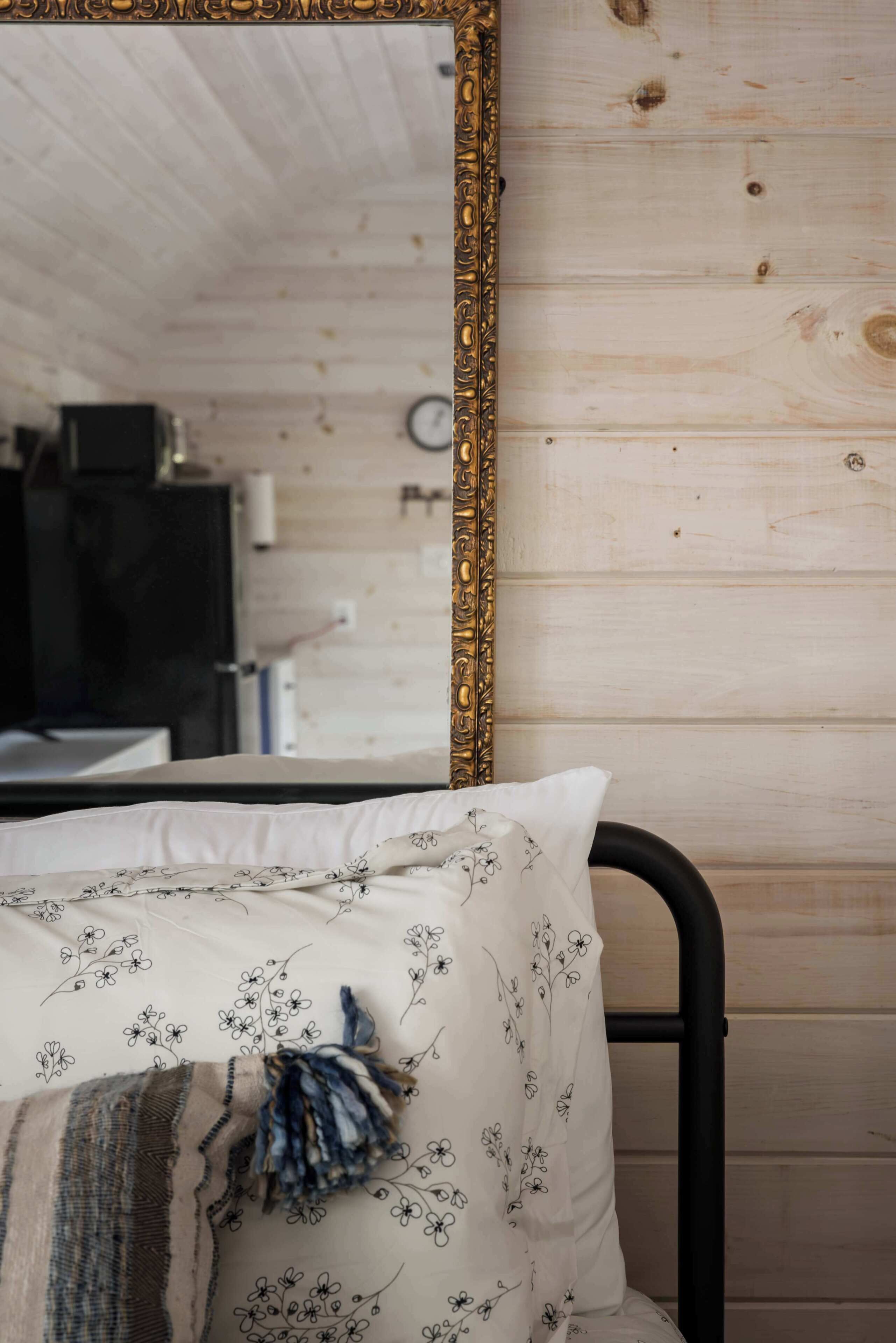 Un lit avec un oreiller à motifs floraux et une couverture, un mur en bois et un miroir doté d’un cadre orné.