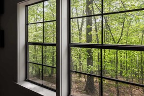 A window with a view of a forested area. - Tiny Cabin w Fire Pit Game Room and Dog Friendly (Great Cacapon)