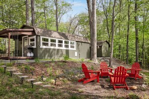 A rustic cabin with a covered porch and a dining area with red Adirondack chairs.
