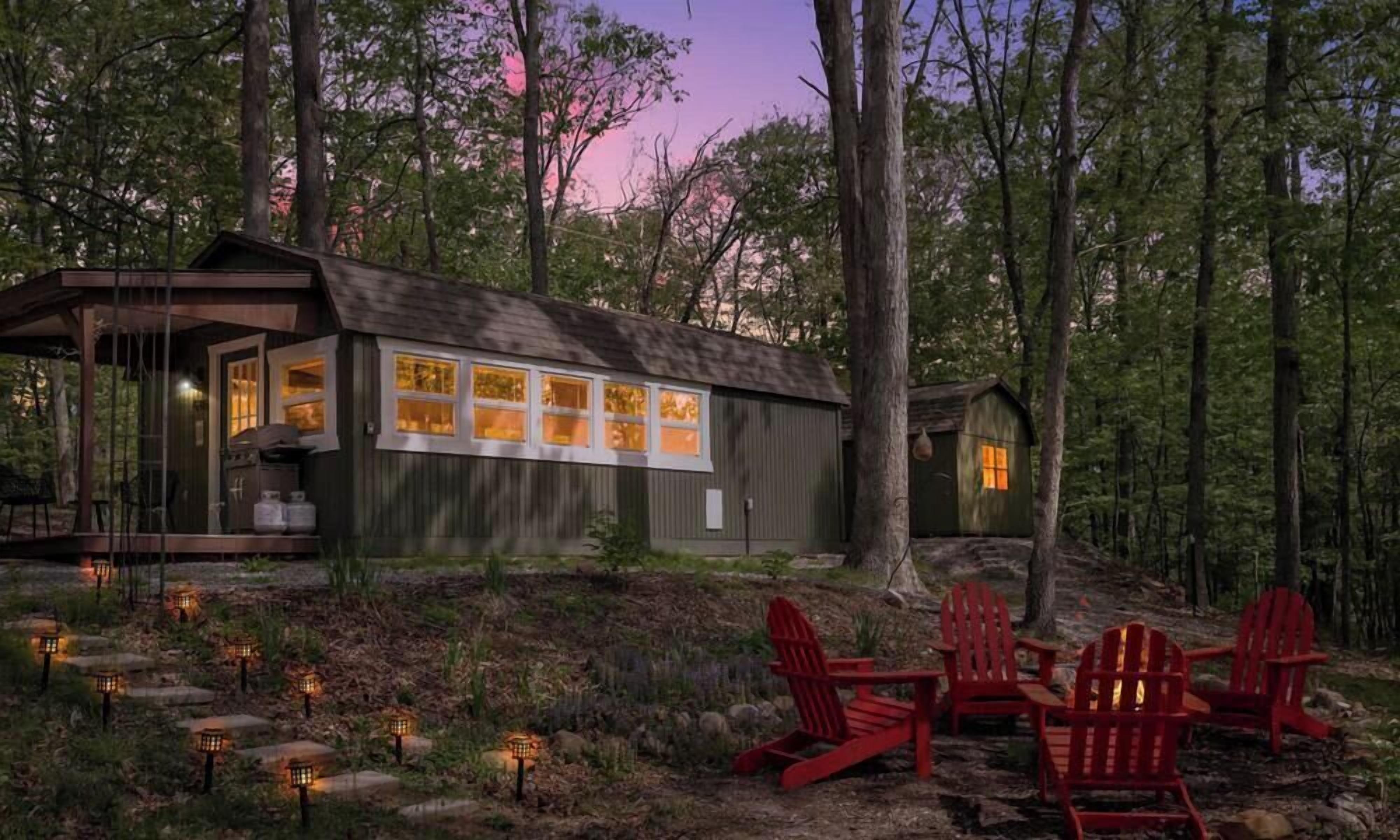 A cabin with a deck, surrounded by trees, and outdoor seating.