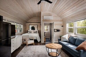 A cozy cabin interior with a bed, a sofa, a desk, and a TV.