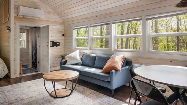 Ein gemütliches Blockhauss-Interieur mit einem blauen Sofa, einem runden Holztisch und großen Fenstern mit Blick auf den Wald.
