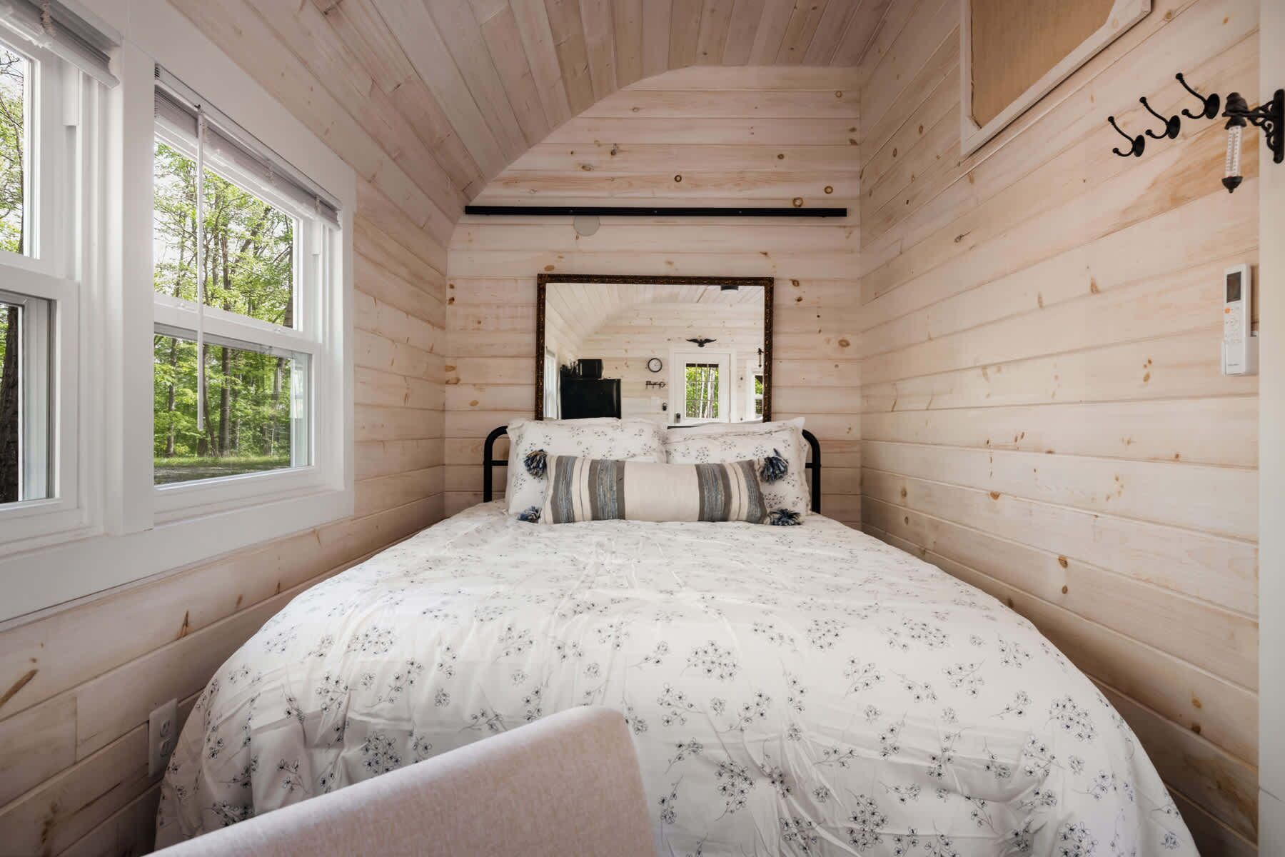 A wooden cabin bedroom with a bed, a window, and a mirror on the wall.