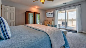 A bedroom with a bed, a ceiling fan, a nightstand, a dresser, a window with a view, and a sign on the wall.