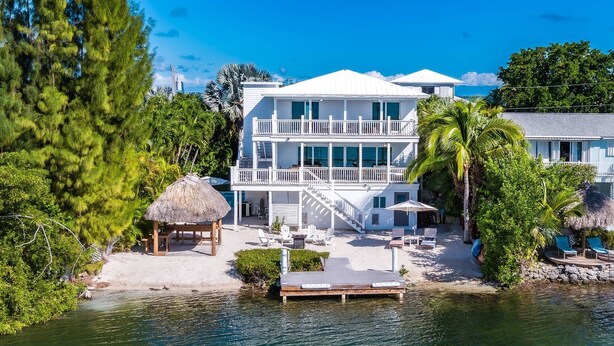 A beachfront hotel with a two-story structure, a covered outdoor seating area, and a dock extending into the water.