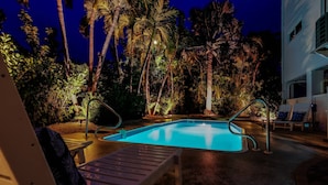 A swimming pool surrounded by palm trees, with a lounge chair and a small table nearby.