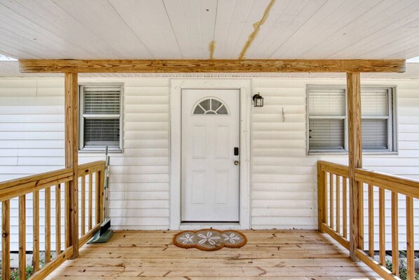 A wooden porch with a white door, two windows with shutters, and a doormat.