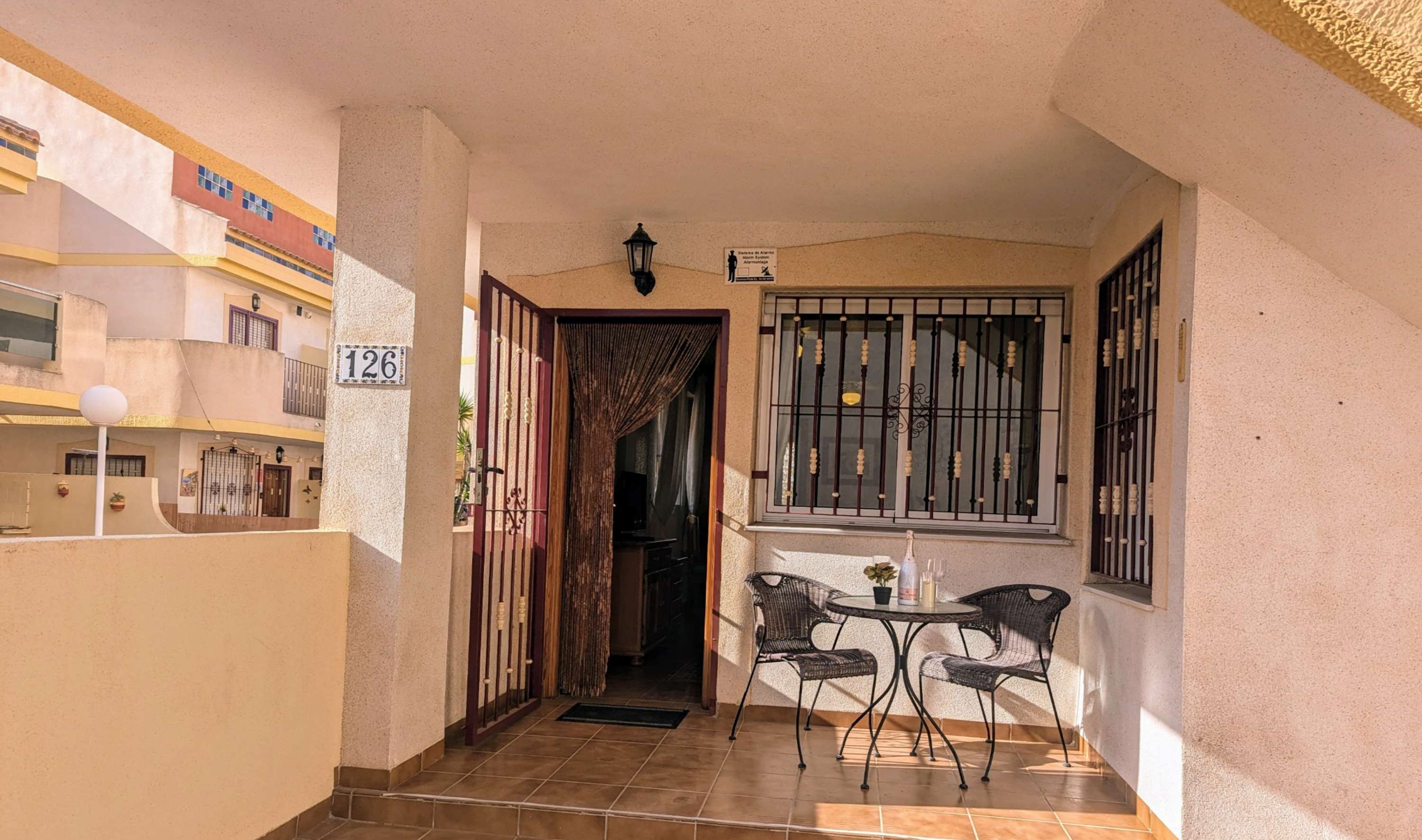 A corridor with a tiled floor leading to a balcony with a table and chairs.