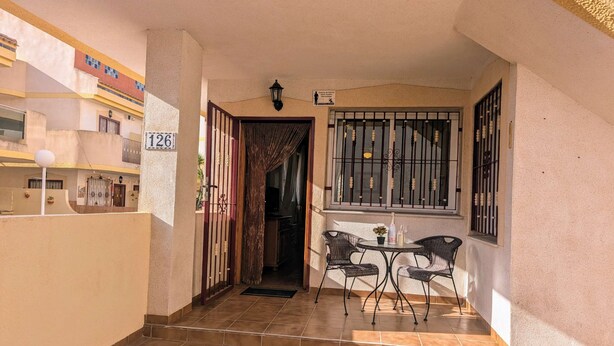 A corridor with a tiled floor leading to a balcony with a table and chairs. - La Zenia Ground-Floor Apt w/ Pool LZ12 (Orihuela)
