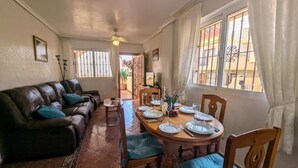A dining area with a wooden table set for four, a leather sofa, and a view through a window with metal bars. - La Zenia Ground-Floor Apt w/ Pool LZ12 (Orihuela)