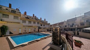 A swimming pool with a tiled deck, surrounded by residential buildings with balconies and satellite dishes. - La Zenia Ground-Floor Apt w/ Pool LZ12 (Orihuela)