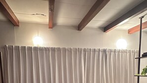 Una habitación con un sofá de cuero marrón, una cortina blanca, piso de madera y una pequeña mesa redonda con una planta.
