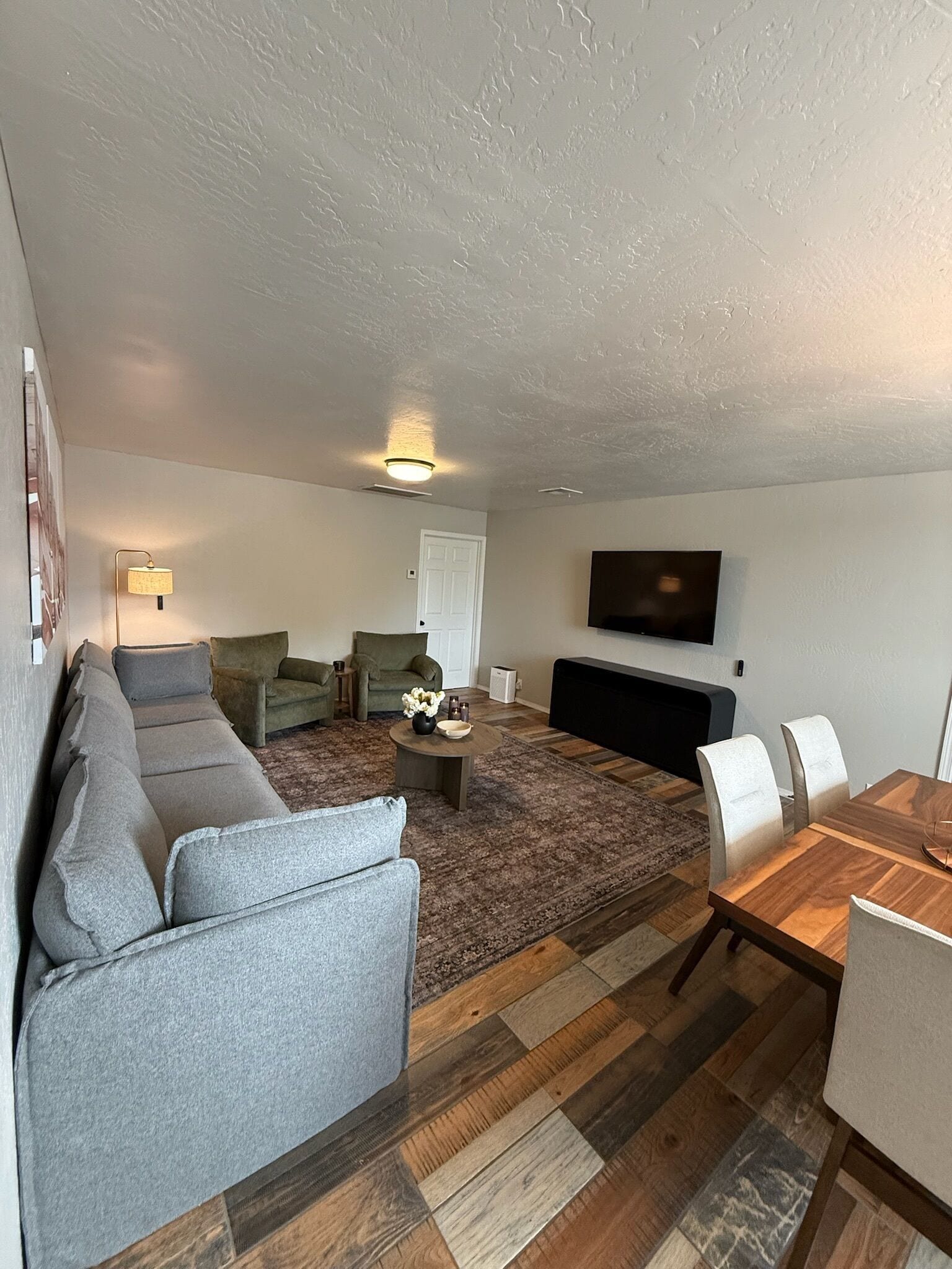 A living room with a sofa, chairs, a coffee table, and a TV mounted on the wall.