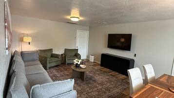 A living room with a sofa, chairs, a coffee table, and a TV mounted on the wall.