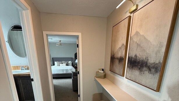 Un pasillo con suelo de madera, una cama al fondo y un cuadro en la pared.