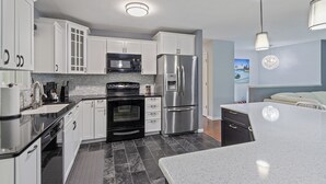 A modern kitchen with white cabinets, stainless steel appliances, a black oven, and a granite countertop.