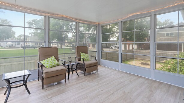 A sunroom with large windows, two armchairs with cushions, a small table, and a view of a backyard.