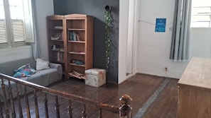 Una habitació amb una escala de fusta, una prestatgeria, una taula petita i una finestra amb persianes.