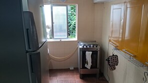Een compacte keuken met een koelkast, oven en raam met uitzicht op groen.