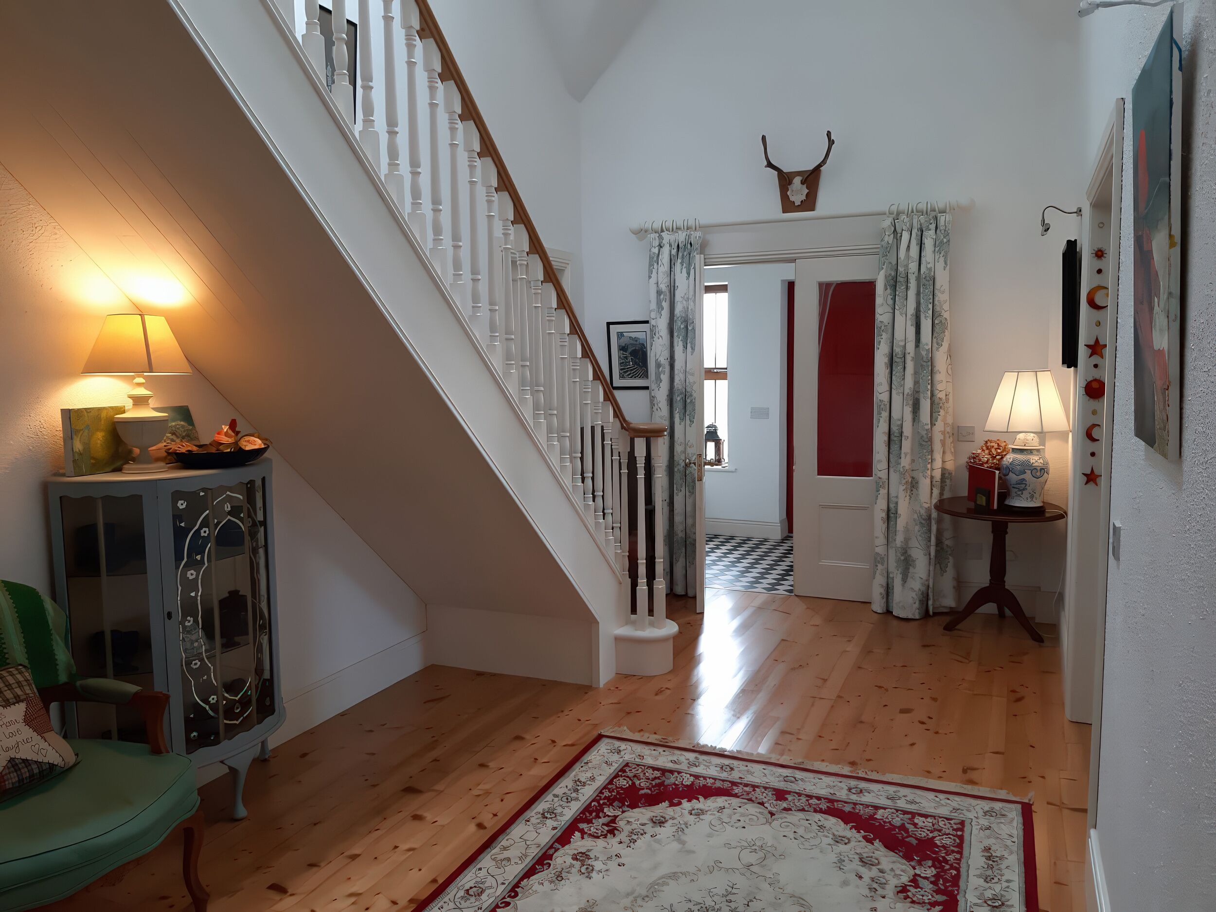 A staircase with white balusters, a red door, and a patterned rug on a wooden floor.