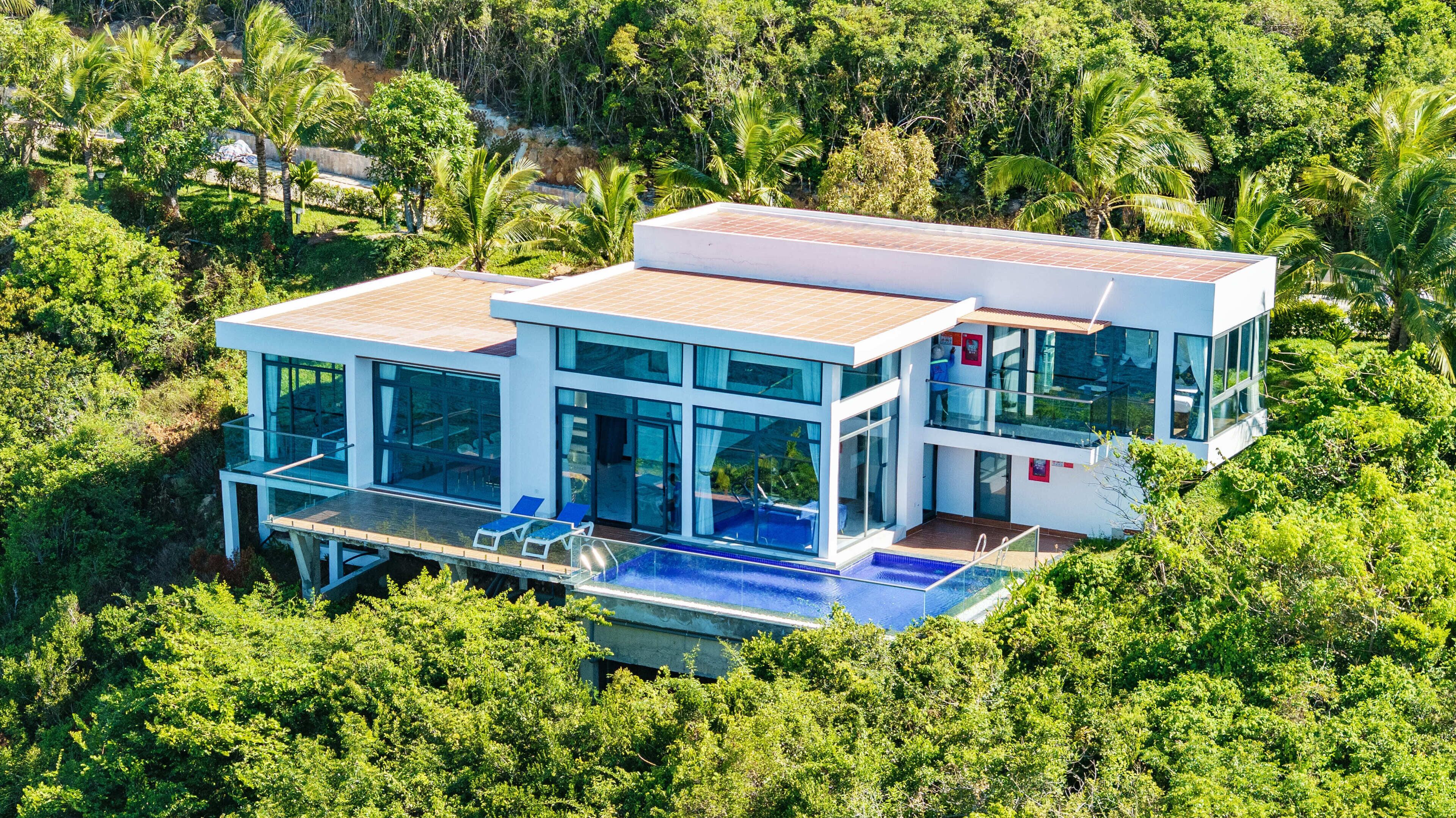 Een modern huis met twee verdiepingen, grote glasramen, een zwembad en een weelderig groen bos eromheen.