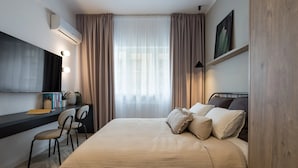 A modern hotel room with a large bed, a desk with a chair, a flat-screen TV, and a large window with curtains. - Downtown Bucharest Studio Close to Cismigiu & Universitatii (Bucharest)