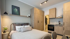 A modern bedroom with a bed, bedside table, and a small plant. Adjacent is a kitchenette with a stove, sink, and cabinets. - Downtown Bucharest Studio Close to Cismigiu & Universitatii (Bucharest)