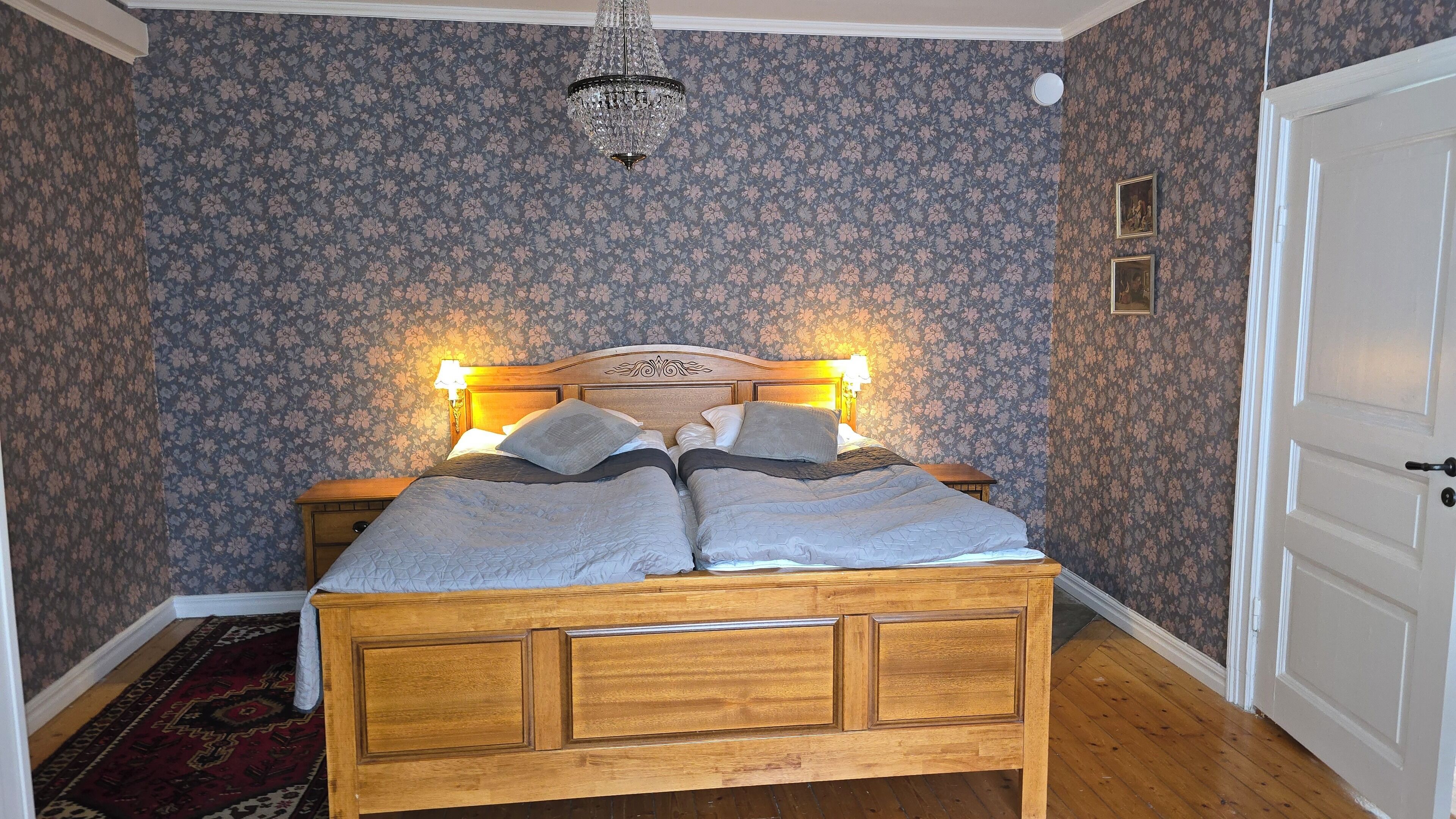 A bedroom with a wooden bed, floral wallpaper, and a chandelier.