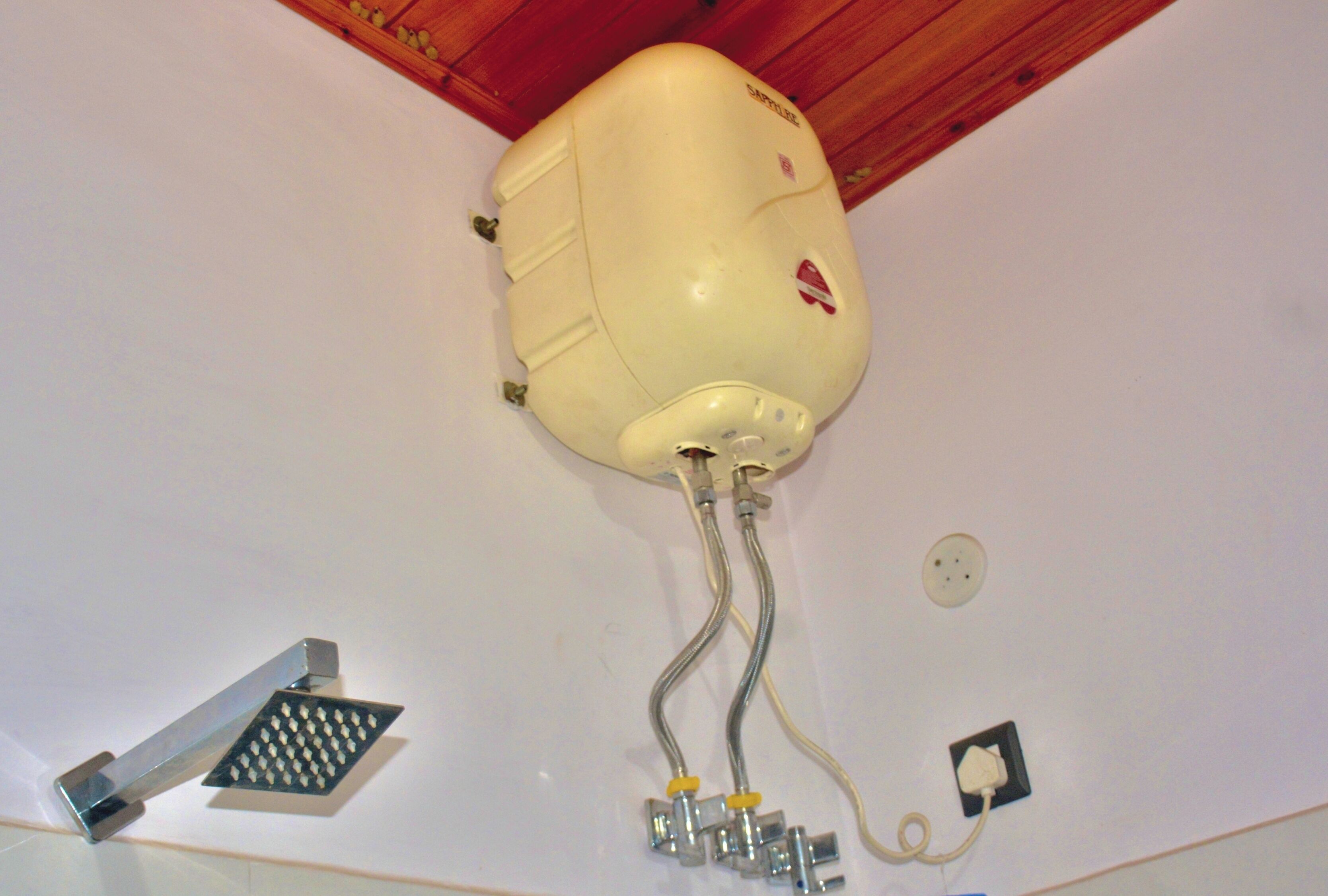 A ceiling-mounted water heater with exposed pipes and a control valve.