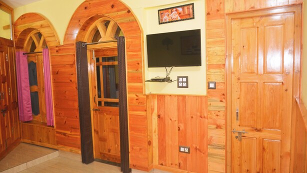 A wooden interior with a television mounted on the wall, a door, and a small shelf with a remote control.