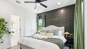 A bedroom with a large bed, a ceiling fan, a nightstand with a lamp, and green curtains. - Spacious 4-bedroom house in lovely Dallas W/Game room & Spa (Dallas)